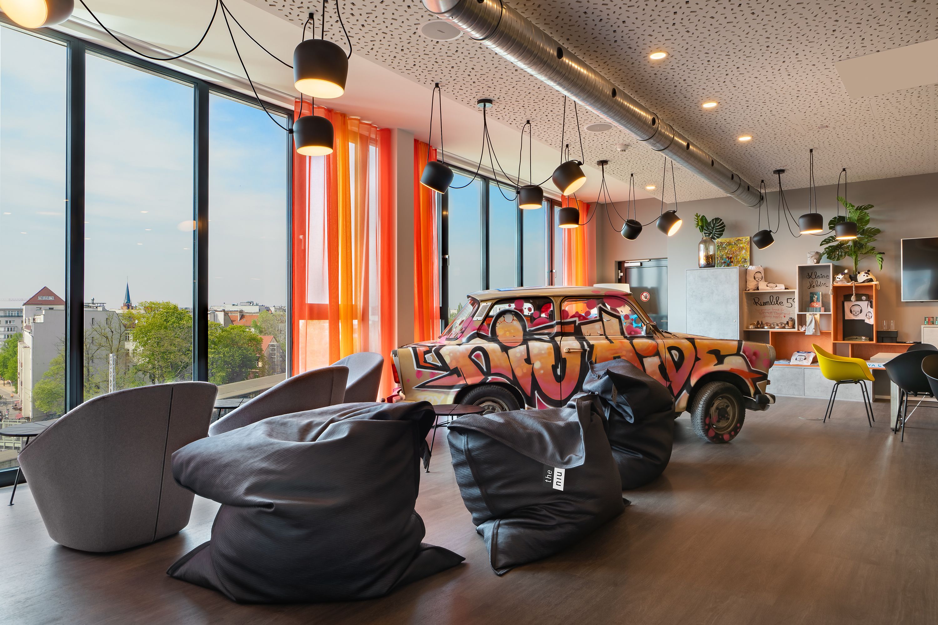 Stylische Lounge im Hotel the niu Hide Berlin mit farbenfrohem Retro-Design, gemütlichen Polstersesseln, DDR-inspirierten Dekoelementen und Blick durch große Fenster auf die Berliner Stadtlandschaft.