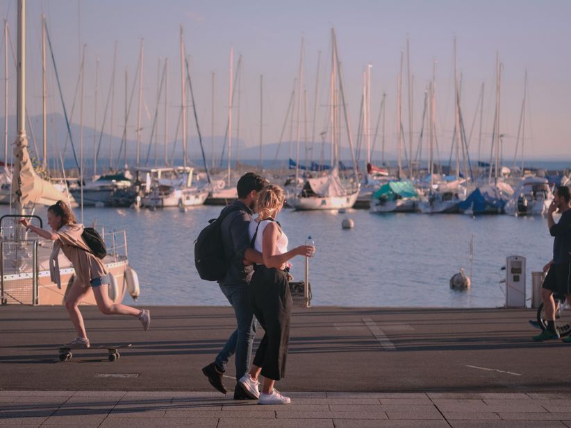 zwei Menschen spazieren an der Promenade des Genfer Sees in Lusanne entlang im Hintergrund sind mehrere Segelboote