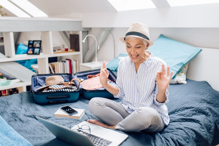 Ältere Frau sitzt auf Bett und plant eine Reise und freut sich