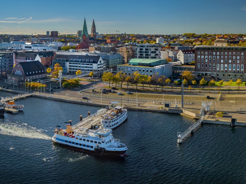 Luftaufnahme von Kiel mit Blick auf die Stadt, die Ostseeküste und ein an der Förde liegendes Kreuzfahrtschiff – maritimes Flair und Hafenatmosphäre aus der Vogelperspektive.