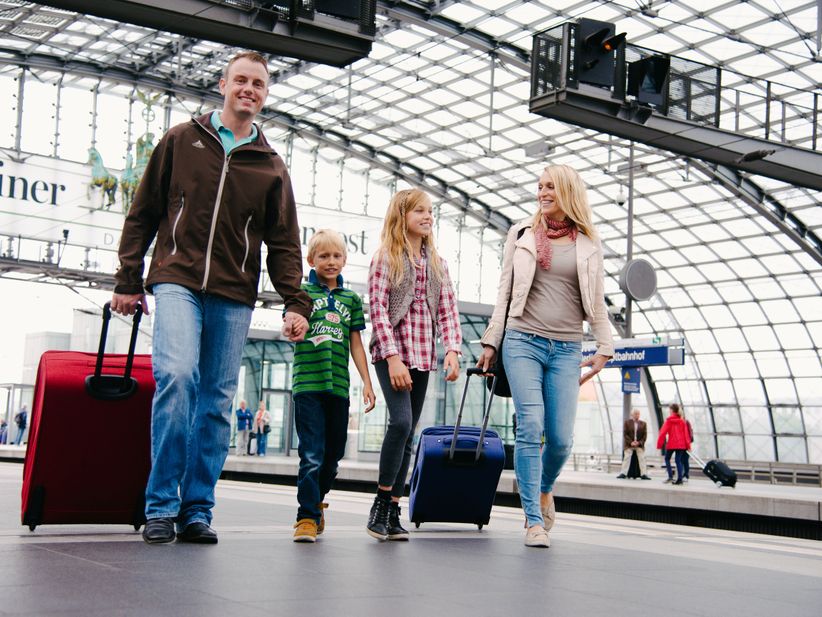 Familie mit zwei Kindern und Koffern gehen am Bahnhof zum Gleis