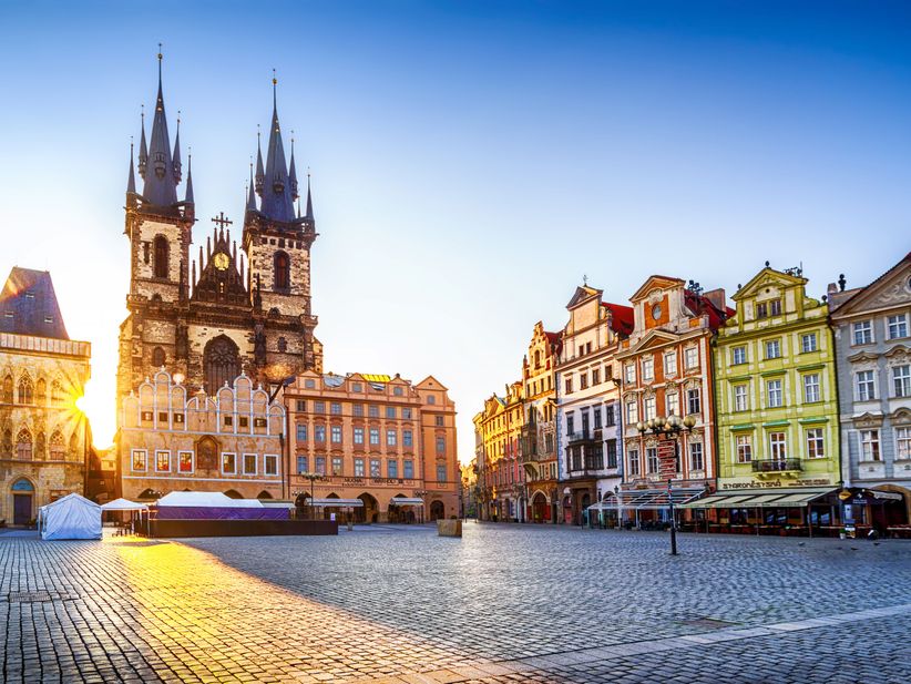 Die Teynkirche in Prag im warmen Licht der Morgensonne, der Platz davor liegt ruhig und ist von historischen Gebäuden gesäumt.