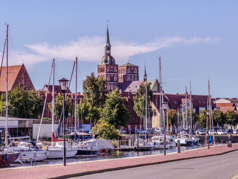Segelboote liegen im Hafen von Stralsund vor historischer Kulisse mit Backsteingebäuden und Blick auf das ruhige Wasser der Ostsee.