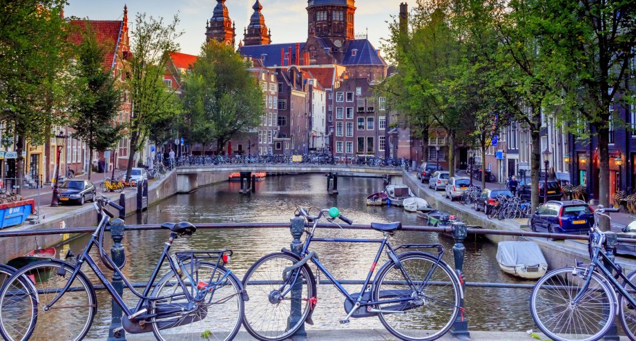 Fahrräder auf einer Kanalbrücke in Amsterdam, im Hintergrund ist die Basilika St. Nikolaus zu sehen - BAHNHIT.DE, © getty, Foto: maydays
