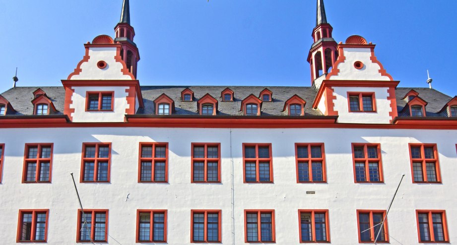 Die rot-weiße Fassade der Johannes Gutenberg Universität vor blauem Himmel in Mainz/Rheinland Pfalz - BAHNHIT.DE, © getty, Foto: TBE