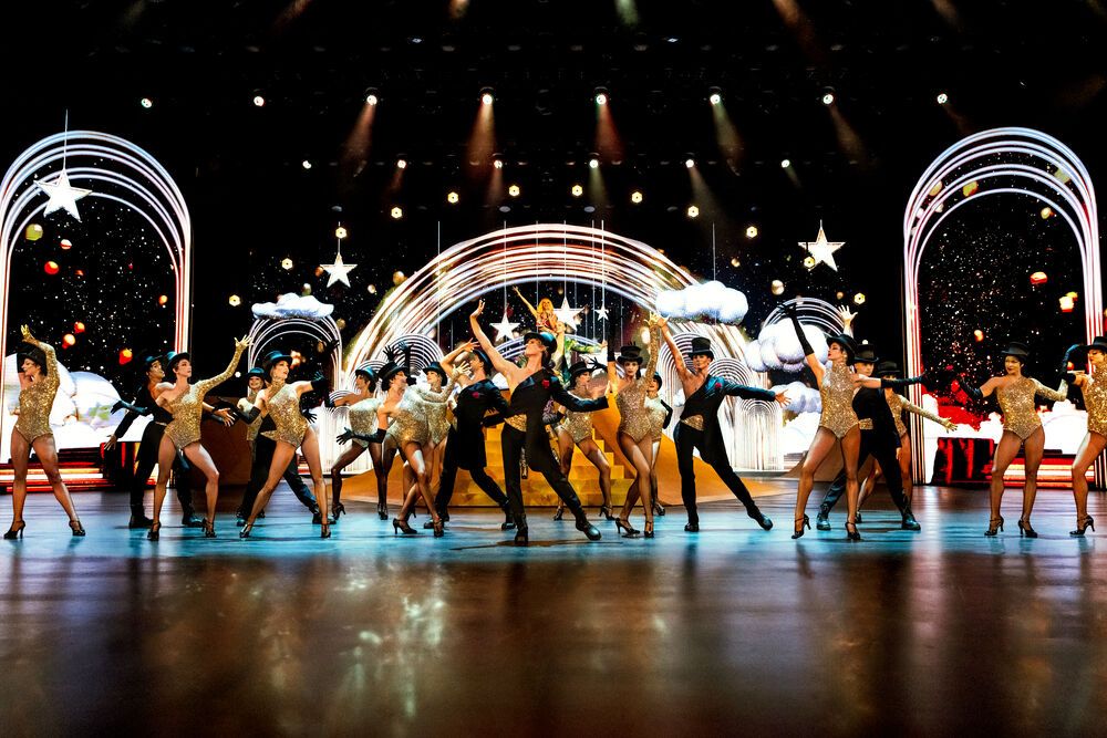 Blinded by Delight Bühnenszene mit vielen Tänzerinnen und Sternen im Hintergrund