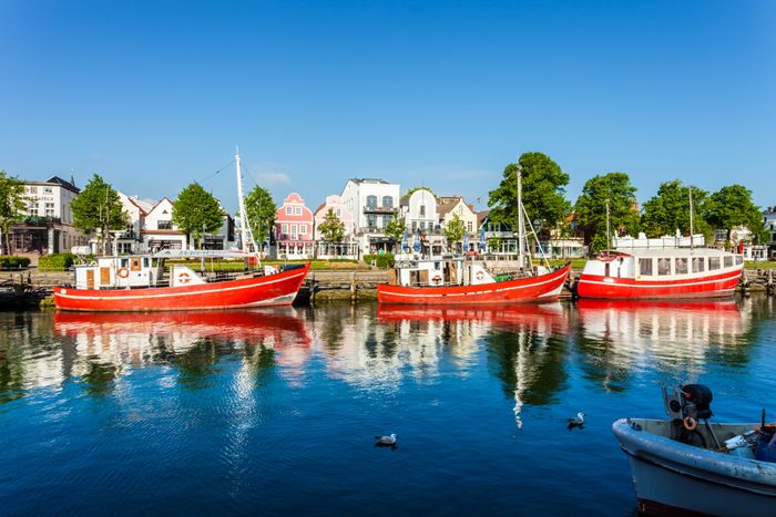 Warnemünde mit Booten im Alten Strom und Blick auf die historischen Häuser entlang der Uferpromenade.