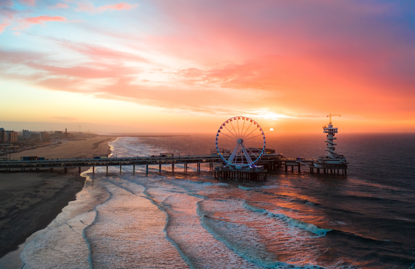Strand von Scheveningen aus der Vogelperspektive mit Pier, Riesenrad und Leuchtturm bei Sonnenuntergang
