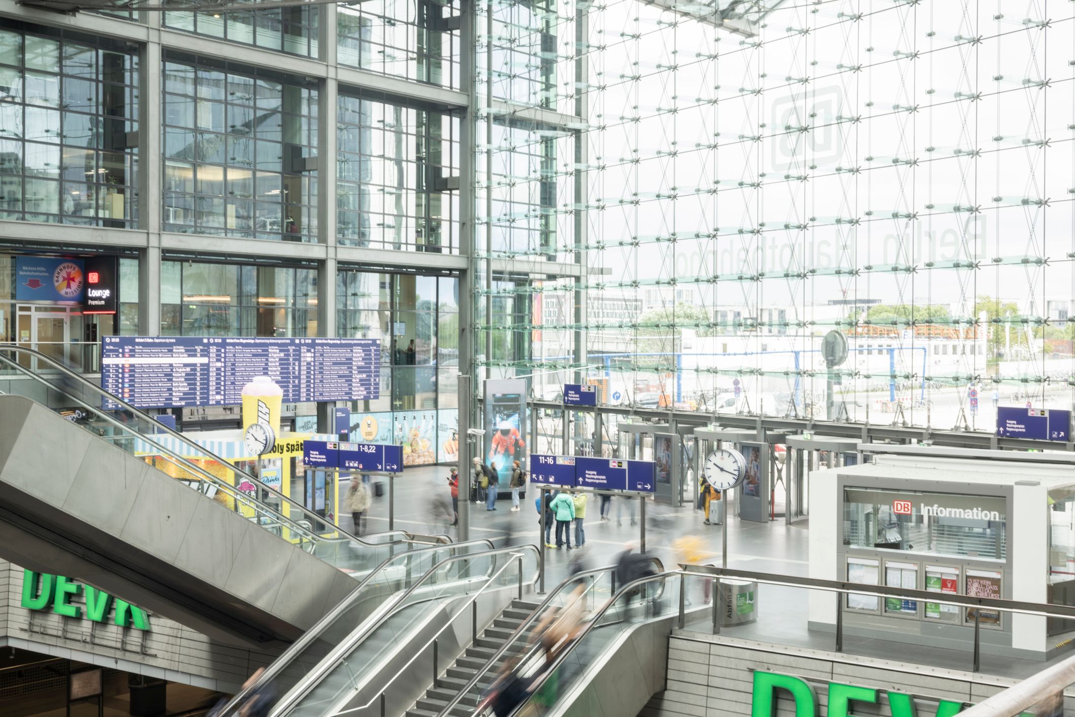 Blick von oben auf eine Rolltreppe und Reisende in der belebten, lichtdurchfluteten Halle des Berliner Hauptbahnhofs.