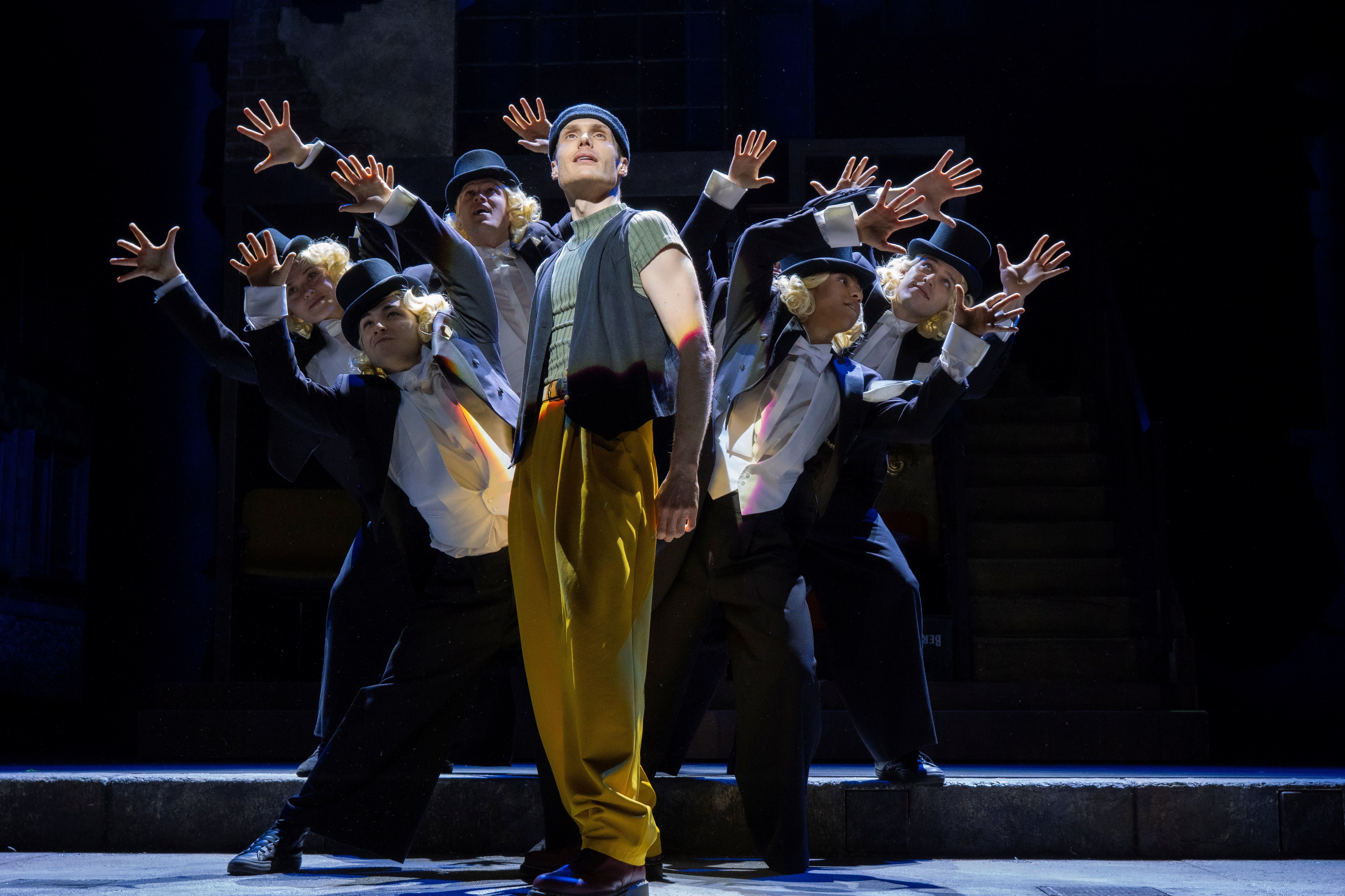 Männlicher Protagonist blickt in die Ferne mit Tänzern im Hintergrund. Bühnenszene des Musicals WIR SIND AM LEBEN im Theater des Westens in Berlin.