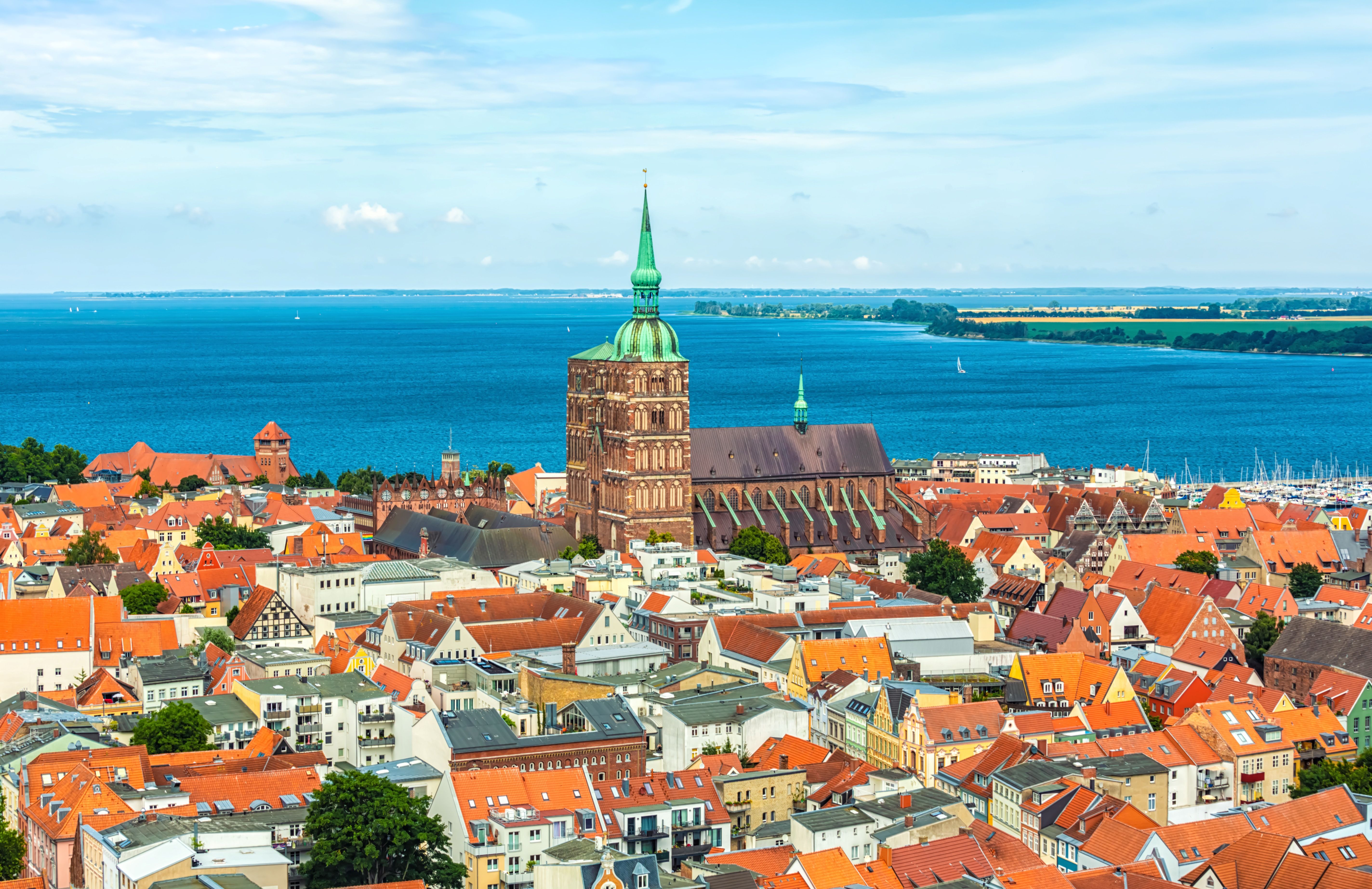 Panoramablick auf die Altstadt von Stralsund mit markantem Kirchturm, roten Backsteindächern und der Ostsee im Hintergrund.