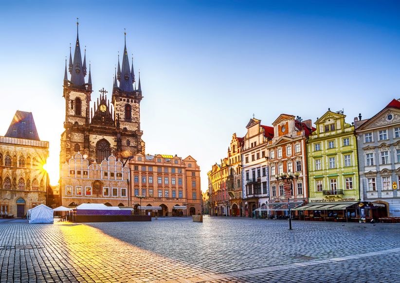 Die Teynkirche in Prag im warmen Licht der Morgensonne, der Platz davor liegt ruhig und ist von historischen Gebäuden gesäumt.